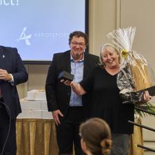 Two men and one woman on stage. The woman received a gift for her long term service.