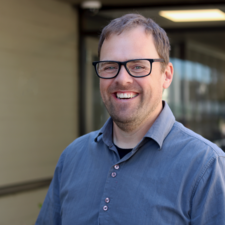 Male wearing glasses and blue shirt smiles for photo