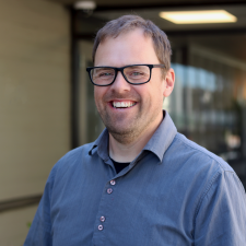 Male wearing glasses and blue shirt smiles for photo