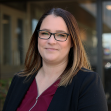 Woman with brown hair wearing red top and black blazer poses for photo