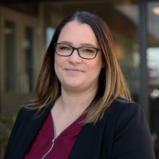 Woman with brown hair wearing red top and black blazer poses for photo